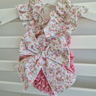 Vestido floral para bebé com laço e volantes pendurado num cabide branco