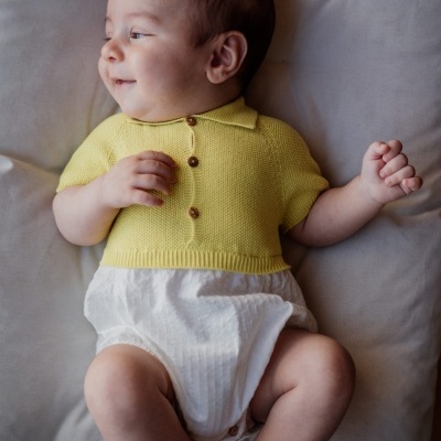 Bebé vestido com camisola amarela e fralda branca deitado num sofá cinzento