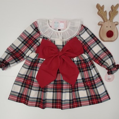 Vestido infantil xadrez com laço vermelho e gola branca ao lado de decoração de rena de madeira