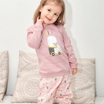 Menina com pijama rosa com desenho de elefante e autocarro, em sofá com almofadas claras.