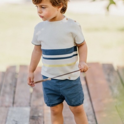 Criança com roupa azul e creme a segurar pau no exterior