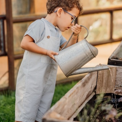 Criança a regar plantas com regador metálico num canteiro de madeira