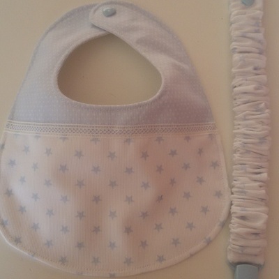 Babete branco com estrelas azuis e prendido de chupeta combinando, com cartão ilustrado ao fundo