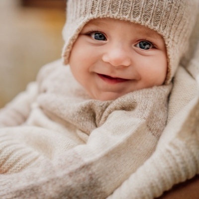 Bebé vestido com roupa de malha bege claro com gorro, sorrindo