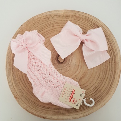 Meia rendada rosa clara com laço e um laço rosa de tecido sobre base de madeira