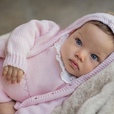 Bebé de roupa rosa de malha deitada numa manta bege