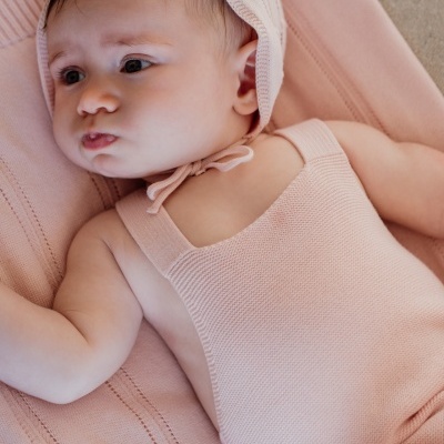Bebé deitado com macacão e gorro de malha rosa