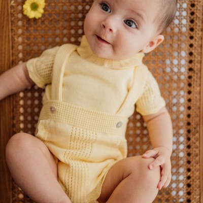 Bebé com roupa amarelo claro sentado numa cadeira de madeira com encosto trançado