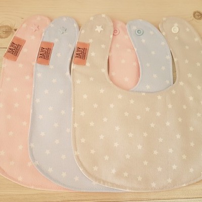 Quatro babetes de tecido com padrão de estrelas em cores pastel sobre madeira clara