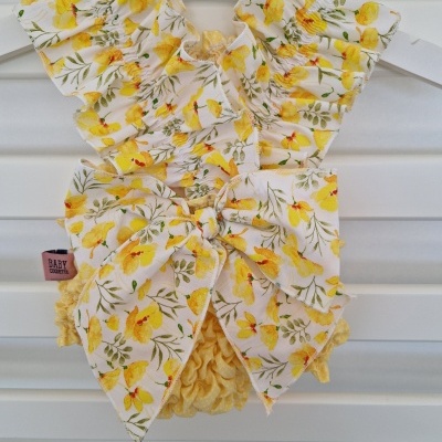 Roupa de bebé floral amarela com laço grande pendurada em cabide branco