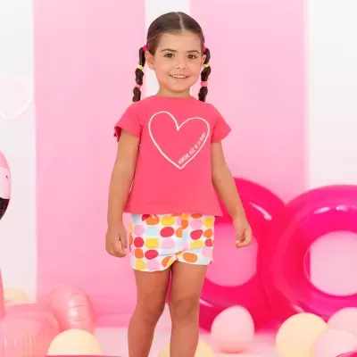 Menina com t-shirt rosa e calções coloridos em ambiente com balões cor-de-rosa