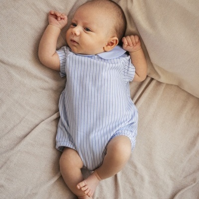 Bebé deitado em tecido bege macio com body riscado azul e branco e gola azul