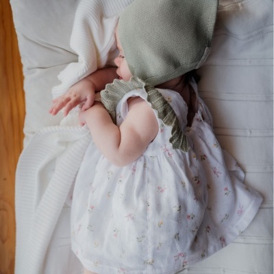 Bebé deitada de lado com vestido branco floral e chapéu verde de malha