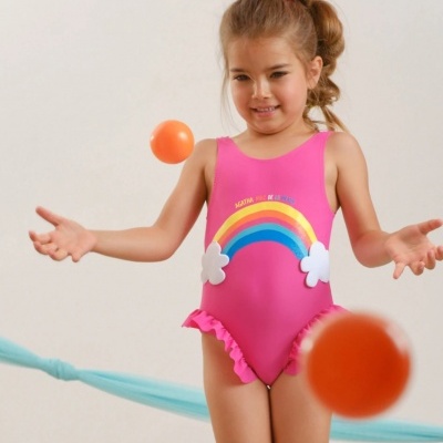 Menina com fato de banho rosa com arco-íris, brincando com bolas laranja