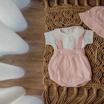 Conjunto de roupa de bebé branco e rosa sobre tapete de ráfia em chão de madeira
