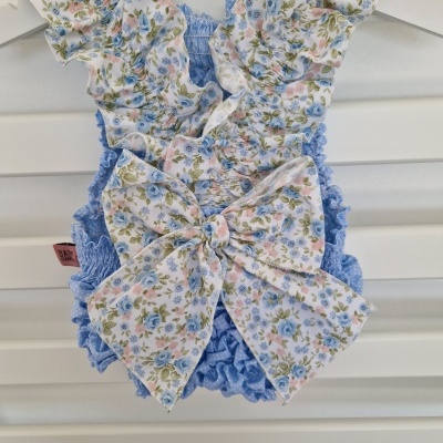 Roupa para bebé azul com padrão floral e laço grande atrás