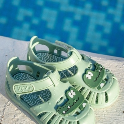 Sandálias infantis verdes com figura de crocodilo e alças ajustáveis junto a piscina