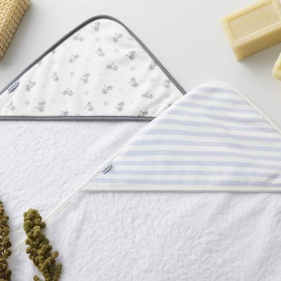 Dois capuzes de toalhas para bebé com padrões de bicicletas e riscas, sobre toalha branca e objetos decorativos próximos.