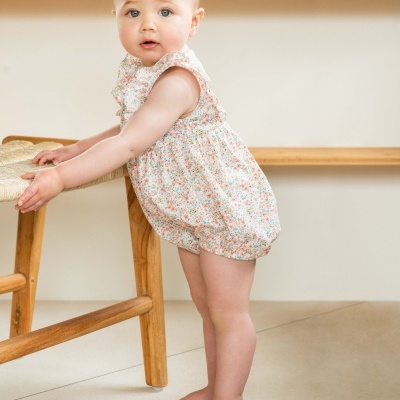 Bebé a usar macacão floral e agarrar banco de madeira