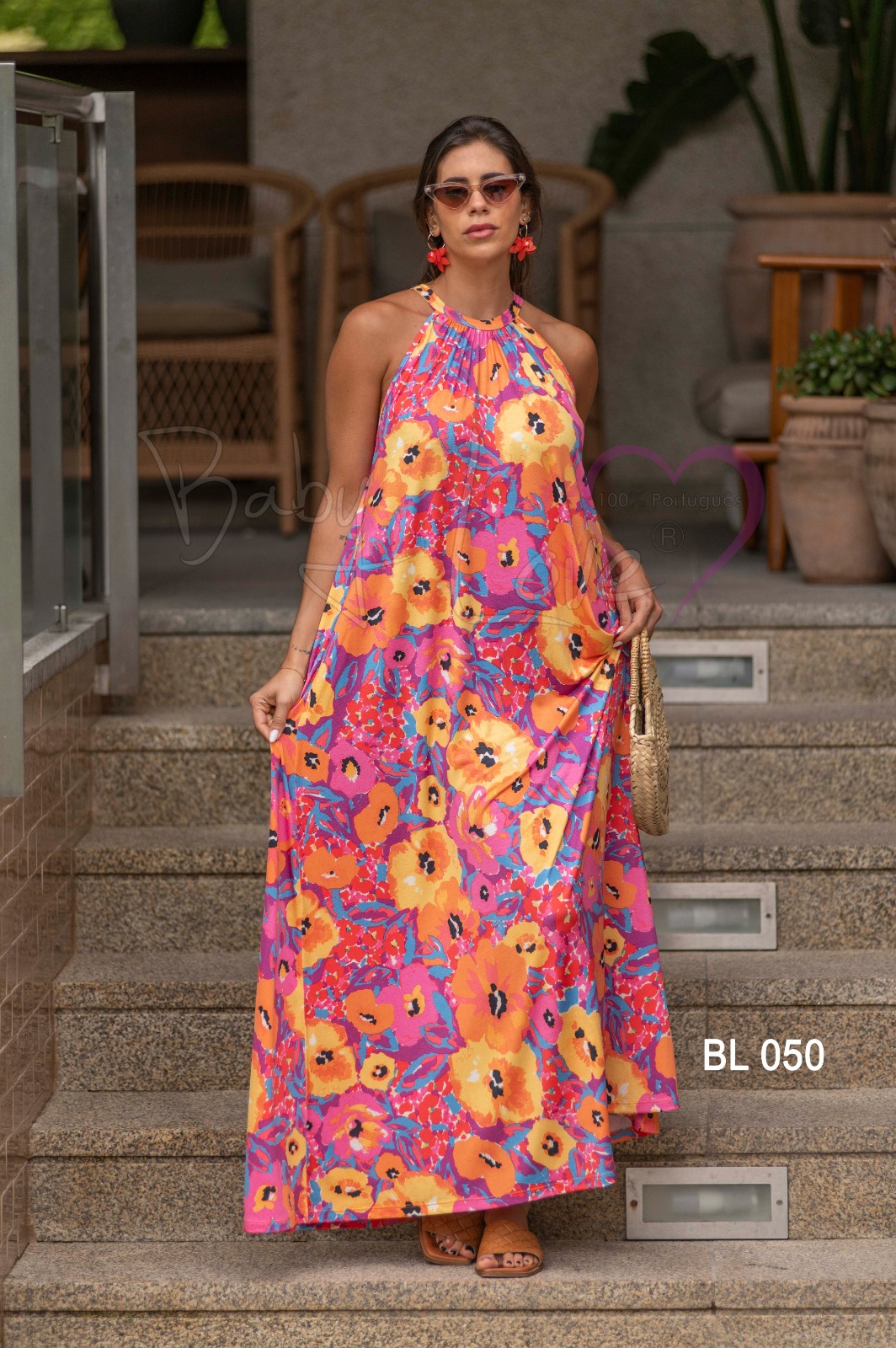 VESTIDO COMPRIDO PADRÃO FLORAL Vestido longo halter floral rosa e laranja usado por mulher com acessórios, em escadas exteriores