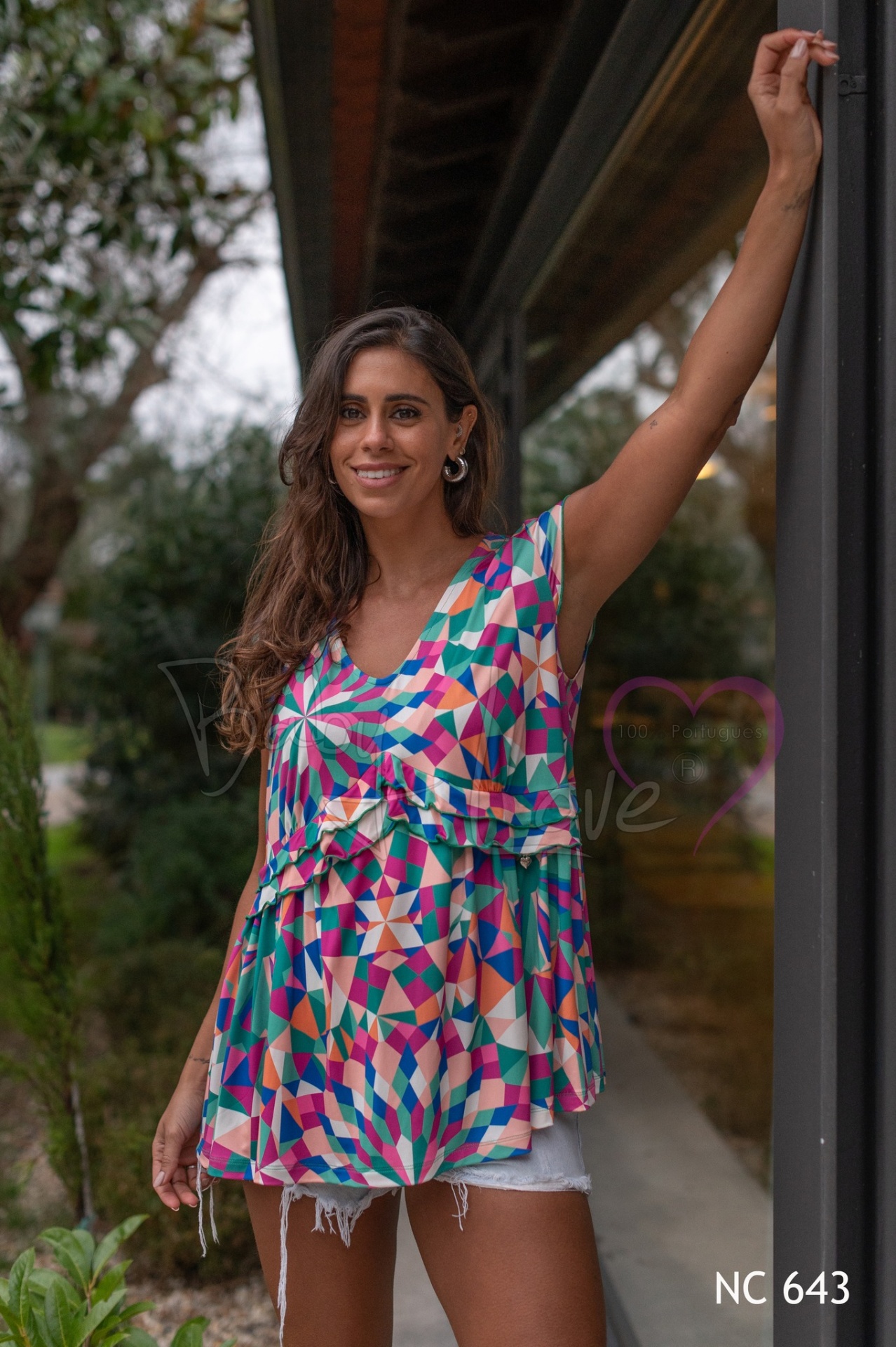 TÚNICA PADRÃO GEOMÉTRICO Mulher a usar blusa colorida geométrica e calções de ganga ao ar livre