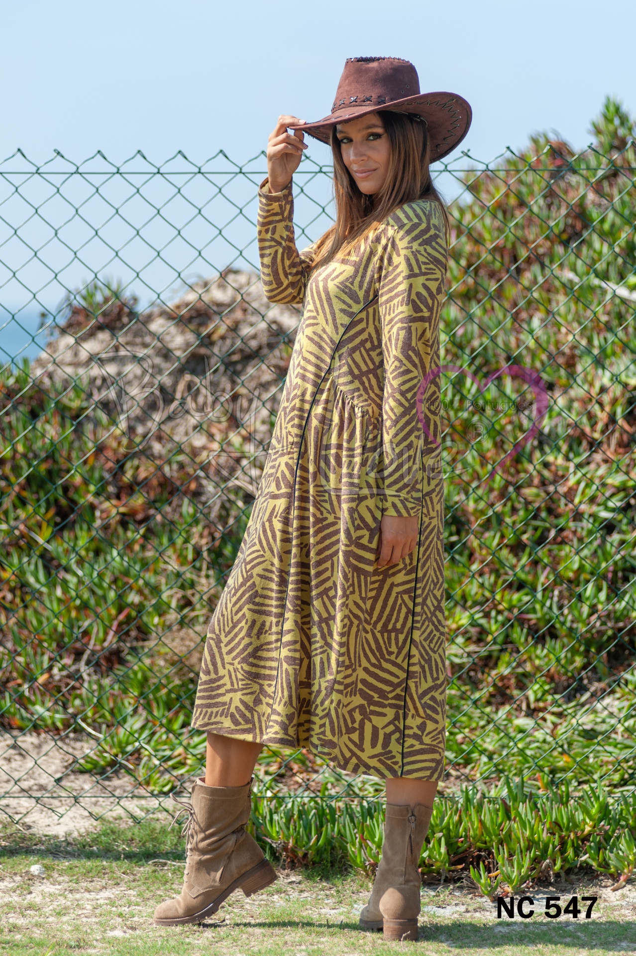 VESTIDO Mulher com vestido comprido estampado, botas e chapéu castanho em área exterior