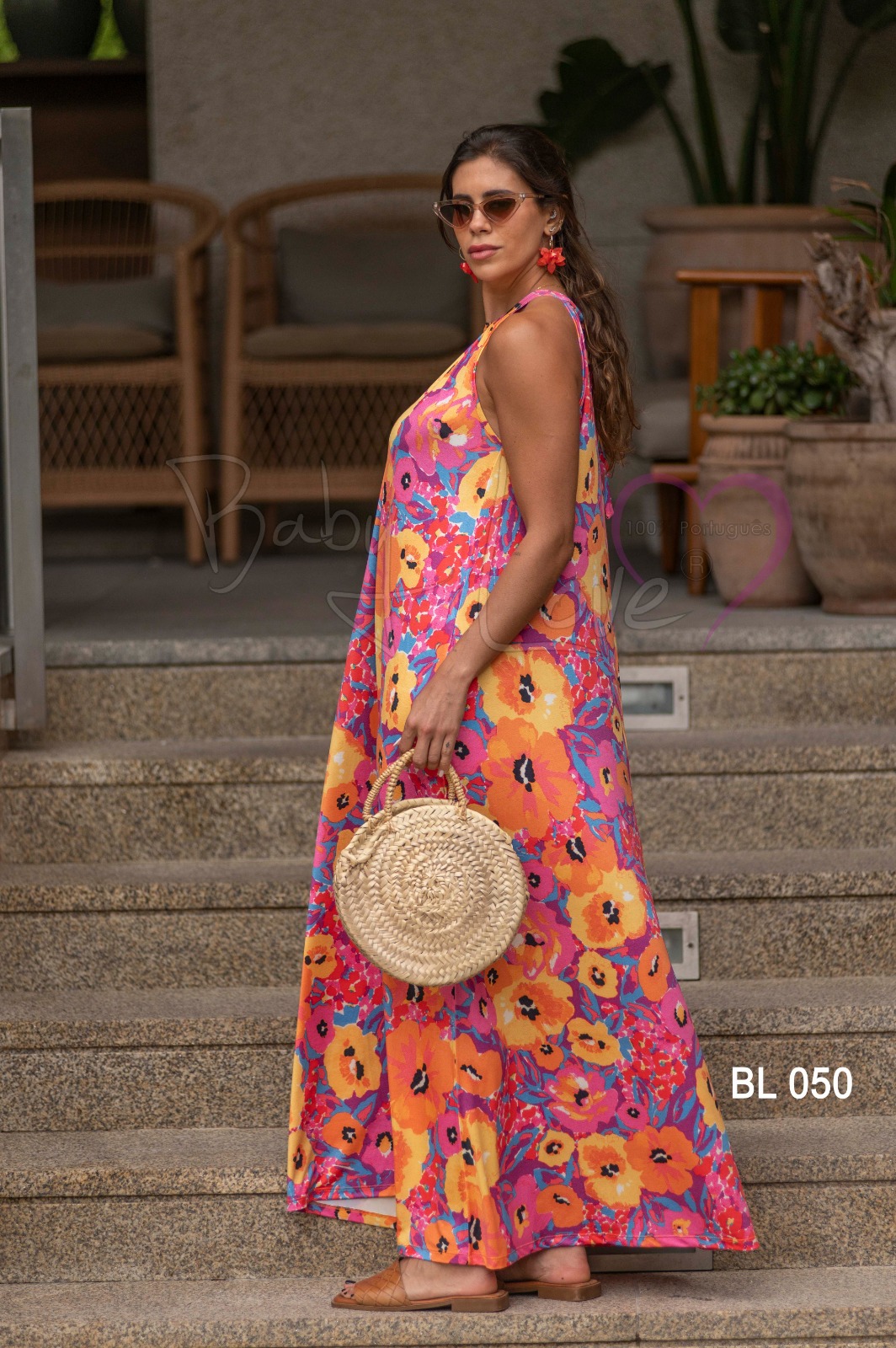 VESTIDO COMPRIDO PADRÃO FLORAL Mulher com vestido floral colorido, bolsa redonda de palha e óculos de sol numa escadaria