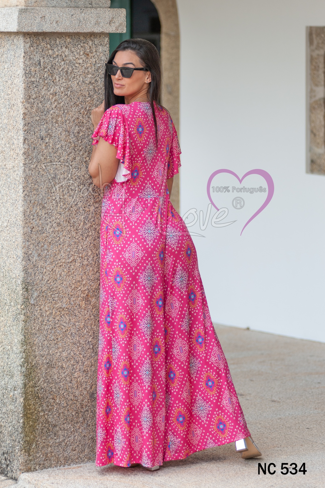 MACACÃO MANDALAS C/NÓ Vestido longo cor-de-rosa com padrão geométrico usado por mulher com óculos de sol, texto '100% Portuguesa', 'Noce Love', 'NC 534'.