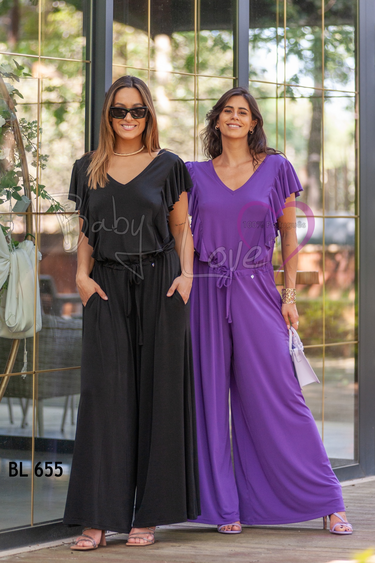 MACACÃO LISO C/ FOLHO Duas mulheres com macacões fluídos em preto e roxo em ambiente com porta de vidro