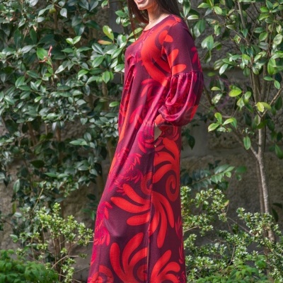 Vestido comprido vermelho e bordô com padrão floral e botas castanhas ao ar livre.