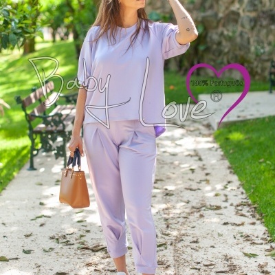 Mulher com conjunto lilás de calça e sweat ao ar livre, segura bolsa castanha