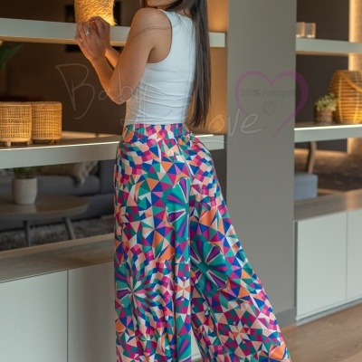 Mulher com pantalonas coloridas e top branco em ambiente interior com prateleiras e plantas