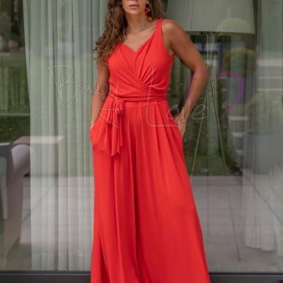 Mulher com vestido vermelho longo com faixa na cintura em varanda com cortinas brancas e candeeiro