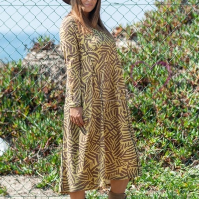 Vestido comprido com padrão geométrico castanho e bege, botas e chapéu castanhos ao ar livre