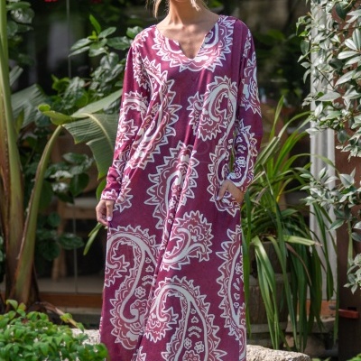 Vestido comprido bordeaux com padrão paisley branco usado com botas bordeaux em ambiente exterior com plantas