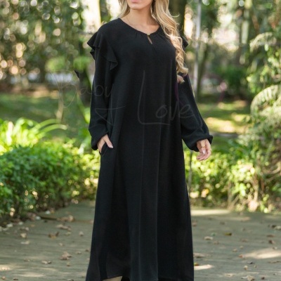 Mulher usando vestido comprido preto com folhos nos ombros e botas brancas ao ar livre