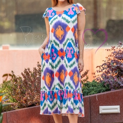 Mulher de vestido midi colorido com padrão geométrico, mangas curtas e volantes na bainha ao ar livre