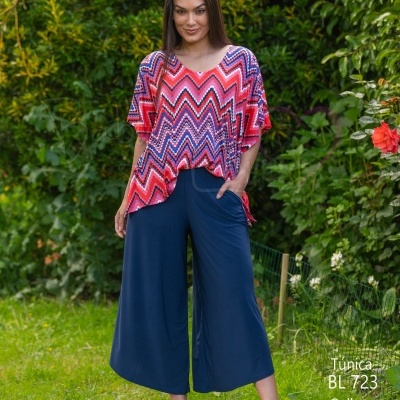 Mulher a usar túnica colorida e calças culotte azuis num jardim