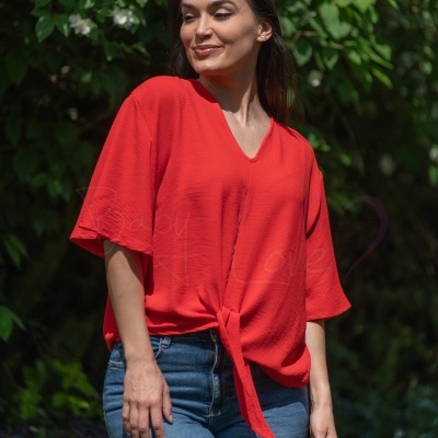 Blusa vermelha texturizada com nó frontal e decote em V, usada por mulher com calças de ganga, fundo com vegetação verde