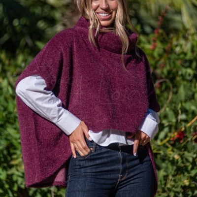 Mulher com capa roxa felpuda e gola alta em ambiente exterior com vegetação