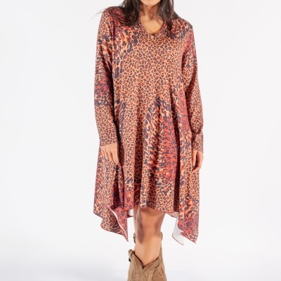 Mulher usando vestido assimétrico com padrão animal print vermelho e castanho, boina vermelha e botas castanhas.