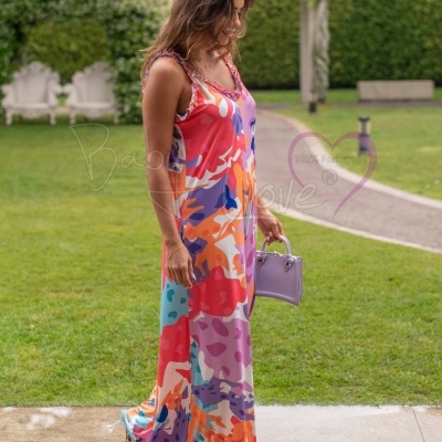 Vestido longo colorido com padrão abstrato e mala lilás num jardim