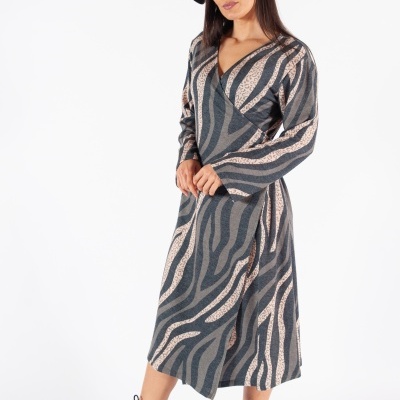 Mulher com vestido comprido cinza com padrão bege, botas pretas e chapéu preto