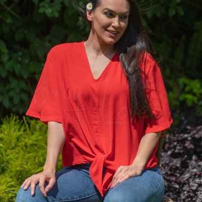 Mulher com blusa vermelha e calças de ganga sentada em cadeira ao ar livre
