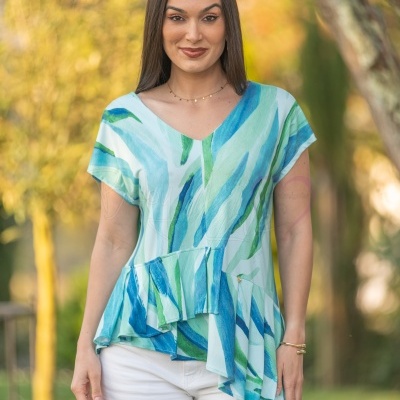 Mulher a usar blusa azul e verde com calças brancas num parque.
