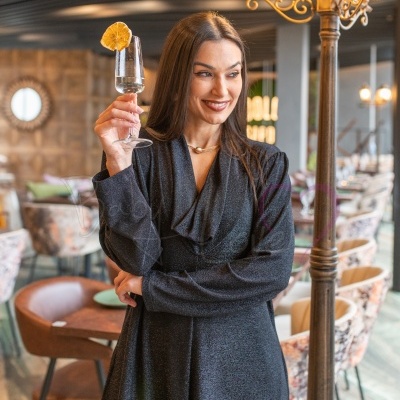 Mulher com vestido comprido preto brilhante a segurar taça de copo com limão seco num restaurante moderno
