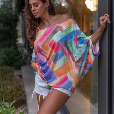 Mulher com t-shirt colorida com padrão geométrico e calções de ganga brancos ao lado de porta de vidro