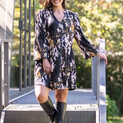 Mulher com vestido curto estampado animal print e botas pretas em escadas ao ar livre.
