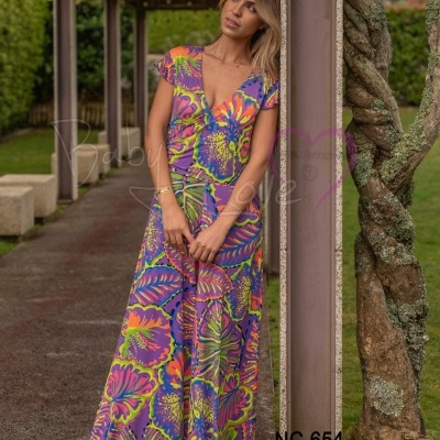 Mulher com vestido longo estampado floral colorido ao lado de coluna de jardim