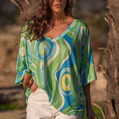 Blusa feminina colorida com padrão abstrato e corte solto em cenário exterior com palmeiras.